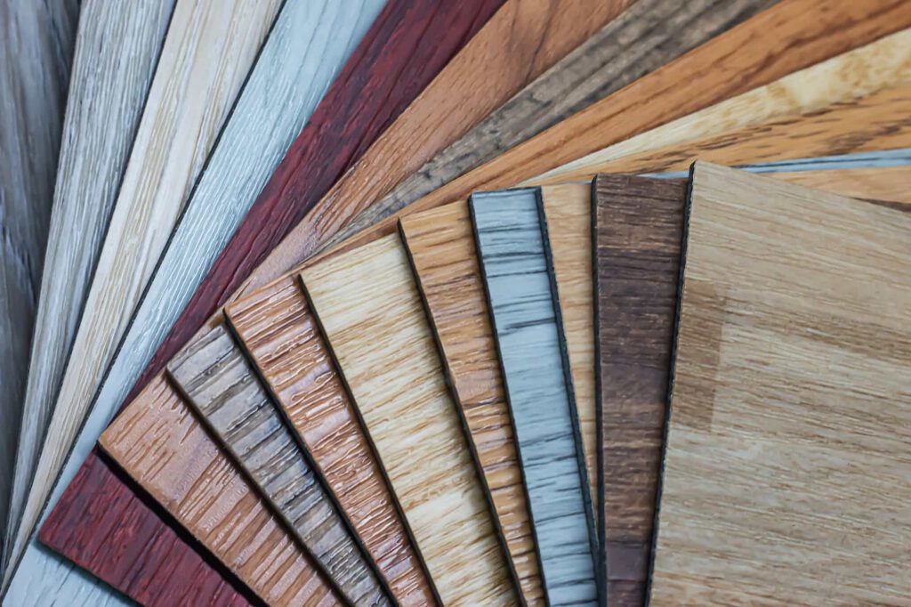 A variety of wood laminate flooring samples arranged in a fanned-out pattern, showing different colors, wood grains, and finishes.